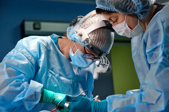 Surgeon performing cosmetic surgery in hospital operating room. Surgeon in mask wearing loupes during medical procadure. Breast augmentation