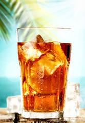 Table background with ice tea on a wooden table top with beautiful blue sky and ocean and palm tree view.