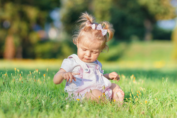 Cute little girl sits on the green grass, outdoors, summer time, blurred background