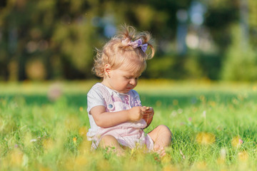 Cute little girl sits on the green grass, outdoors, summer time, blurred background