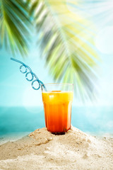 Table background with orange ice juice in a glass on a wooden table top with beautiful blue sky and ocean and palm tree view.