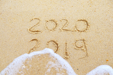 Happy new year. 2020 and 2019 written on the sand where 2019 is getting washed away by the wave