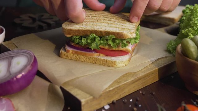 Chef finalizes the sandwich with ham and salad on the wooden board in the beam of light, chef's hand finalizes the sandwich, making of the fastfood at the kitchen, Full HD Prores HQ 422