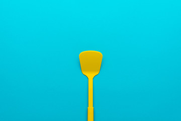 Top view of vivid plastic kitchen utensil. Minimalistic flat lay image of yellow spatula over turquoise blue background with copy space. Central composition of turning spatula on blue table.