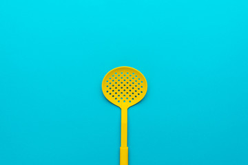 Top view photo of vivid plastic kitchen utensil. Minimalistic flat lay image of yellow skimmer spatula over turquoise blue background with copy space and central composition.