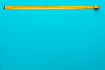 Top view of yellow soft measuring tape. Minimalist flat lay image of tape measure with metric scale over turquoise blue background with copy space.