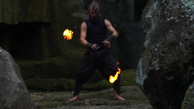 A man with fire in his hands on the background of stones and a waterfall.
