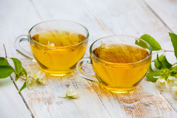 Two cups of green tea with jasmine flowers on grunge wooden table
