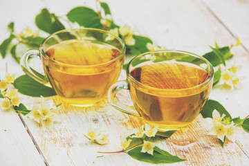 Two cups of green tea with jasmine flowers on grunge wooden table