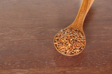 Brown flax seed in spoon on wooden background.
