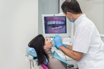 Dentist examining teeth with camera, looking on screen