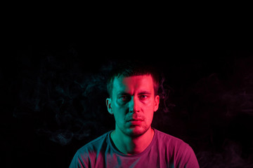 Close-up of face of an unshaven head of a caucasian man looking forward with stubble in the dark, illuminated on one side in Blue and on the other pink on a black isolated background. Cyberpunk style