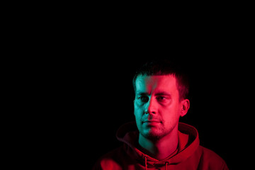 Close-up of the face of an unshaven head of a caucasian man looking away with stubble in the dark, illuminated on one side in Blue and on the other pink on a black isolated background. Cyberpunk style