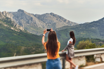 Fototapeta na wymiar Back view of young girls taking pictures of mountains in Valencia community, Spain.