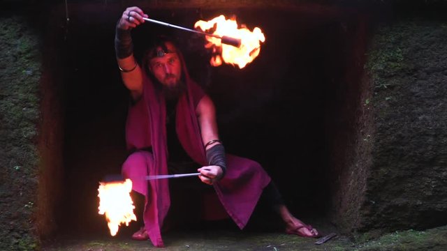 A man with a long beard in a cave with fire in his hands. magical video shooting with fire.