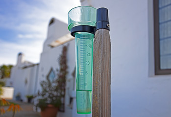 Green rain gauge with building in background