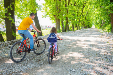 Obraz premium Father and daughter ride bikes in the Park on a Sunny day. Dad teaches the child Cycling.