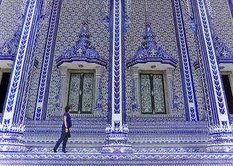 Asian female traveller wearing dark blue shirt and sunglasses walking pass beautiful windows of blue ceramic church in wat pak nam khaem nu temple