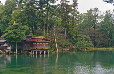 Fototapeta na wymiar Wooden waterfront historic brown and gold pavilion in the clear green fresh water pond at Kenrokuen garden in Kanazawa Japan
