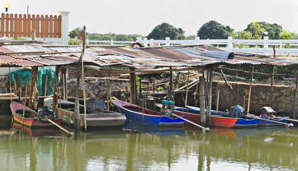 Fototapeta na wymiar Small fisherman long tailed motor boats docked under old zinc plate roofs in the river avoiding sunlight