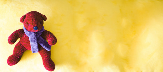 Oso de peluche rojo con bufanda morada sobre fondo amarillo