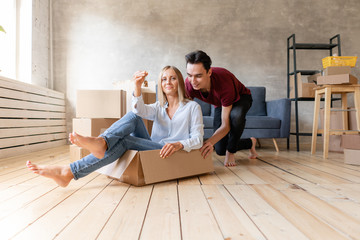 Obraz premium Happy couple having fun and riding in cardboard boxes at new home. Young couple moving to a new apartment together. Relocation concept