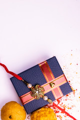 Indian festival – Top view of sweets, elegant Rakhi on blue gift box with spread rice, kumkum and...