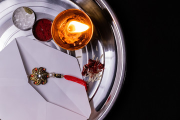 Indian Festival concept- Rakhi in a white envelope with rice grains, kumkum and diya on a plate with black background