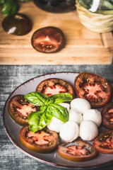 Close up of Italian caprese salad served in plate with basil leaves on rustic table