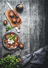 Naklejka na ściany i meble Rustic food background with sliced tomatoes and mozzarella cheese balls. Italian caprese salad with basil leaves on rustic table with ingredients, top view