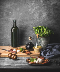 Still life with Italian caprese salad served on rustic table with potted basil kitchen herbs and bottle of olive oil on rustic table with ingredients