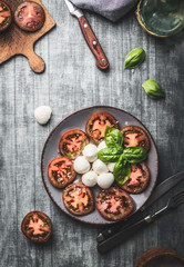 Tomatoes mozzarella balls salad with basil leaves on rustic table with ingredients, top view. Italian caprese salad