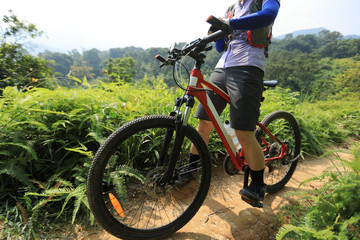 Fototapeta na wymiar Cross country biking woman cyclist set the smartwatch while riding bike in forest on sunny day
