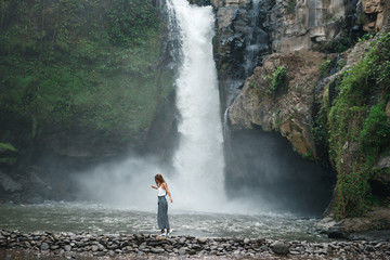 Happy woman near big waterfall traveling at Bali, Ubud. Summer travel at Indonesia. Young Girl in...