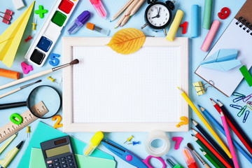 Wooden frame, alarm clock, different stationery and colorful supplies on blue background. Back to school concept. Top view.