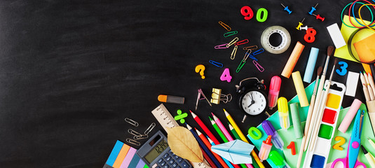 Colorful stationery, alarm clock and supplies on chalkboard background. Back to school concept. Banner format. Top view.