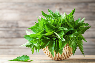 Young nettle leaves in basket on wooden rustic background, stinging nettles, urtica.