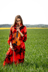 Young woman in red dress with violin in green meadow - image
