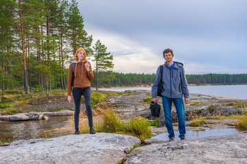 Middle aged man and young lady walking on northern lake shore in summer day. Tourists against...