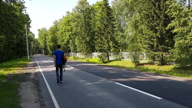 A young man with a limp walks along the road. With a backpack on his shoulders . Travelling alone adult
