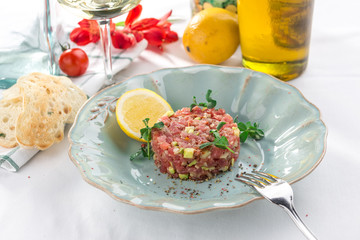 Steak Tartare with bread toasts, lemon and cucumber on white table