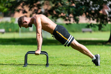 Fit athlete man doing push up with push-up bars on the floor, outdoor  sport and training in grass concepts