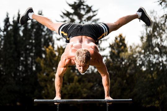 calisthenics hand stand fitness, sport, training and lifestyle concept - young man exercising on parallel bars outdoors