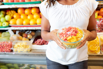 Close-up of young woman holding packed plate with slices of ripe fruits in it while doing shopping in the market