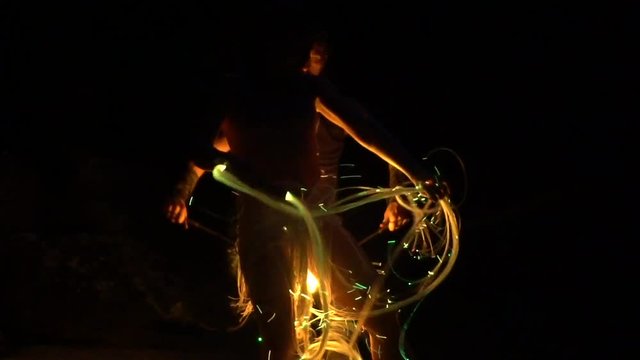 Night video filming of a man with a fire in his hands and a girl with a neon whip.
