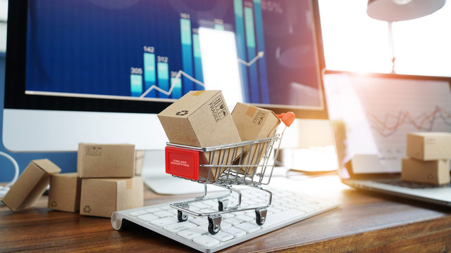 E-commerce. Paper boxes in shopping cart and credit card on keyboard and sales data economic growth graph on computer  screen, online shopping and payments, banking, services online on network.