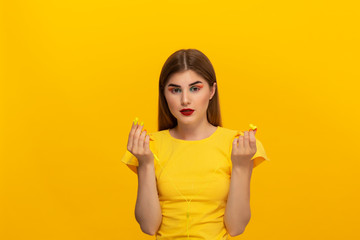 Happy young model in a yellow tee listens to music with wired headphones standing over yellow background