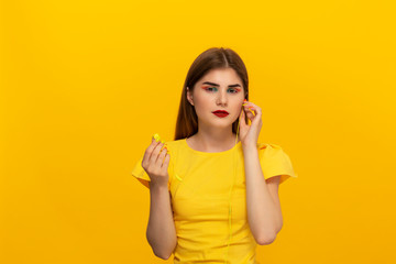 Happy young model in a yellow tee listens to music with wired headphones standing over yellow background