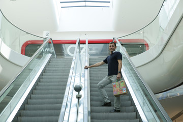 a man rides escalator in a mall with a shopping bag in a New Year's design. Shopping in the mall.