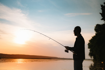 Fisherman at sunset on the river .Beautiful summer landscape with sunset on the river. Fishing. spinning at sunset. Silhouette of a fisherman